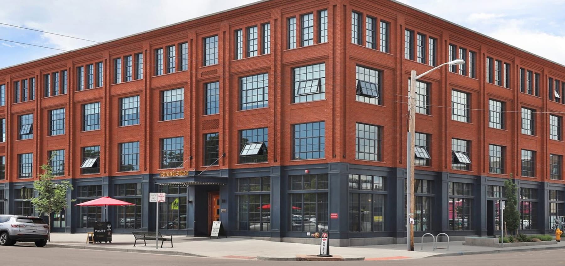 corner-view-of-a-multi-story-red-brick-building-featuring-large-industrial-style-windows-and-storefront-glazing