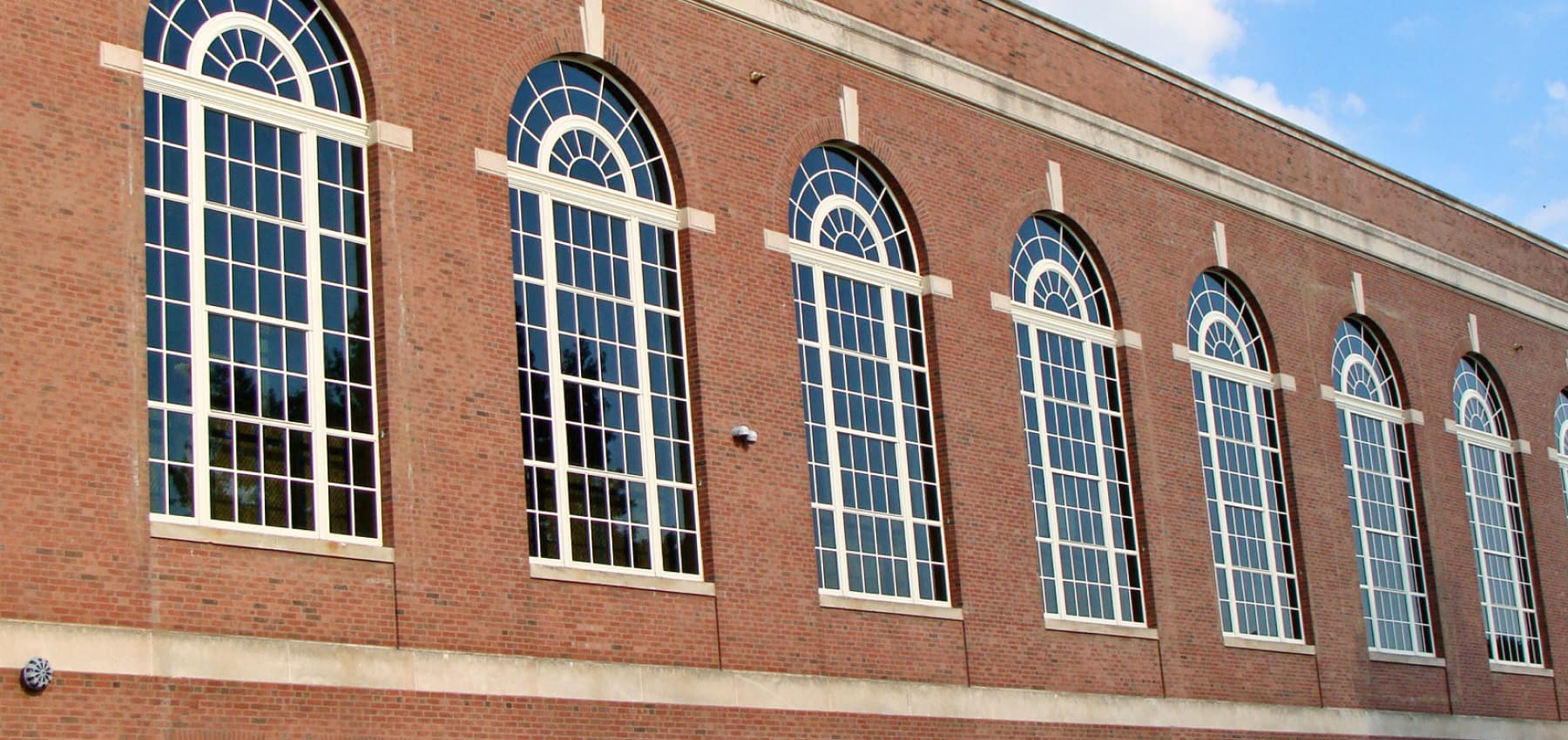 exterior-brick-wall-featuring-a-row-of-tall-arched-windows-with-white-divided-lite-frames-and-fanlight-transoms